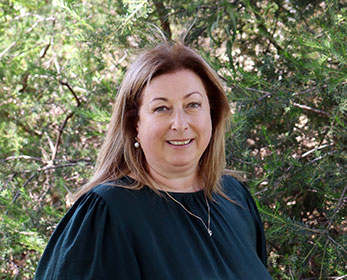 A portrait of Mrs Colette Edmonds-Brown smiling and standing in front of a tree.