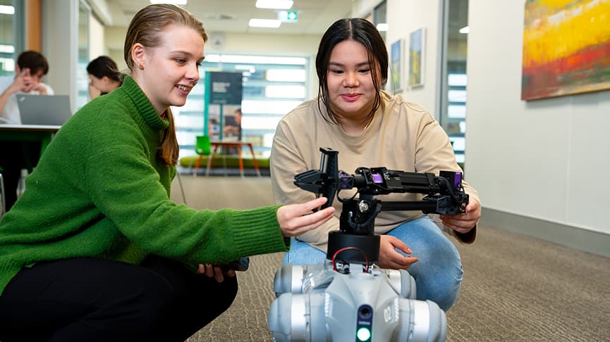 Two students crouch down to work on a robot