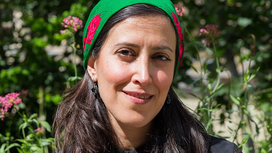 Shirin Barghnavard has wavy black hair, she wears a black blouse and a green and red head piece.