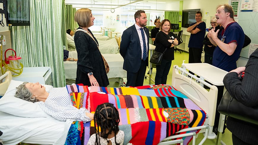 People standing around a bed with a mannequin in it.