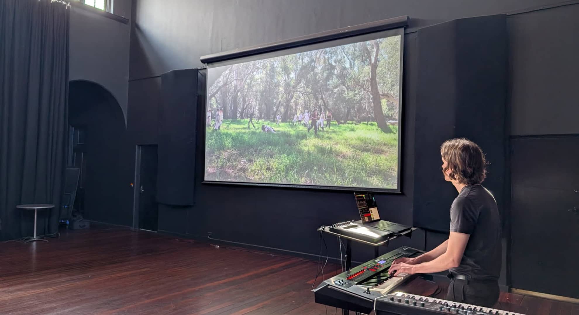 Man plays piano facing a projector screen