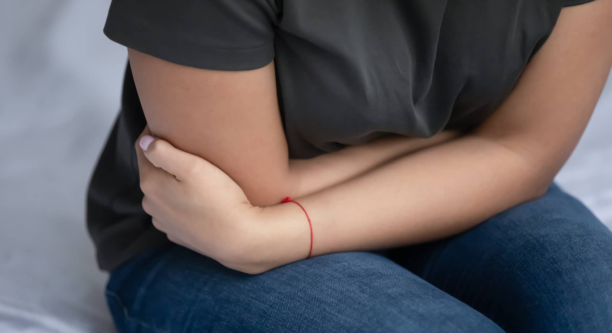 Young woman sitting on a bed clutching her stomach