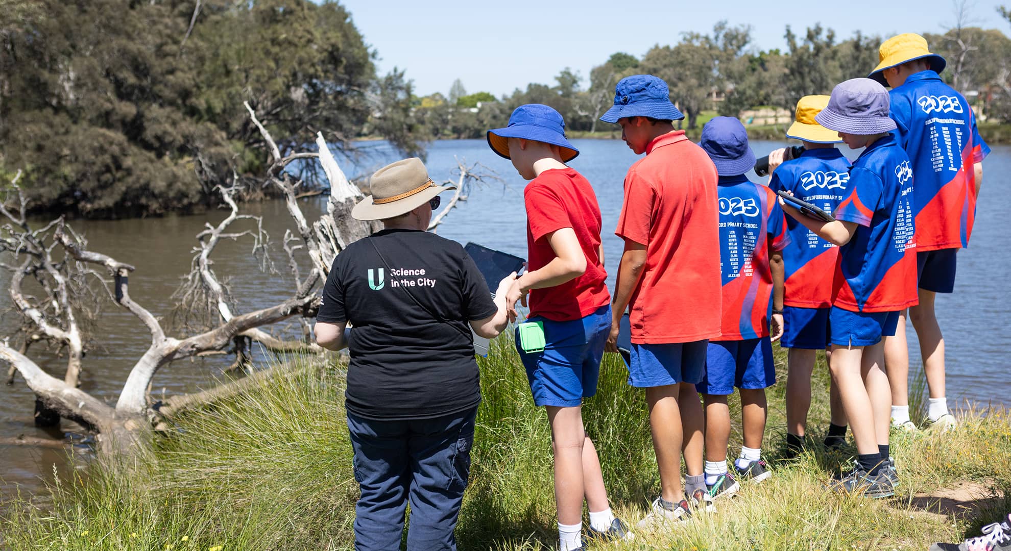 A woman standing with school children in uniform next to a river.