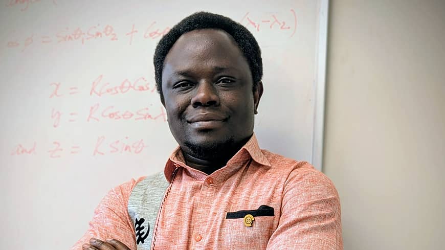 A man in an orange shirt, standing against a white board.
