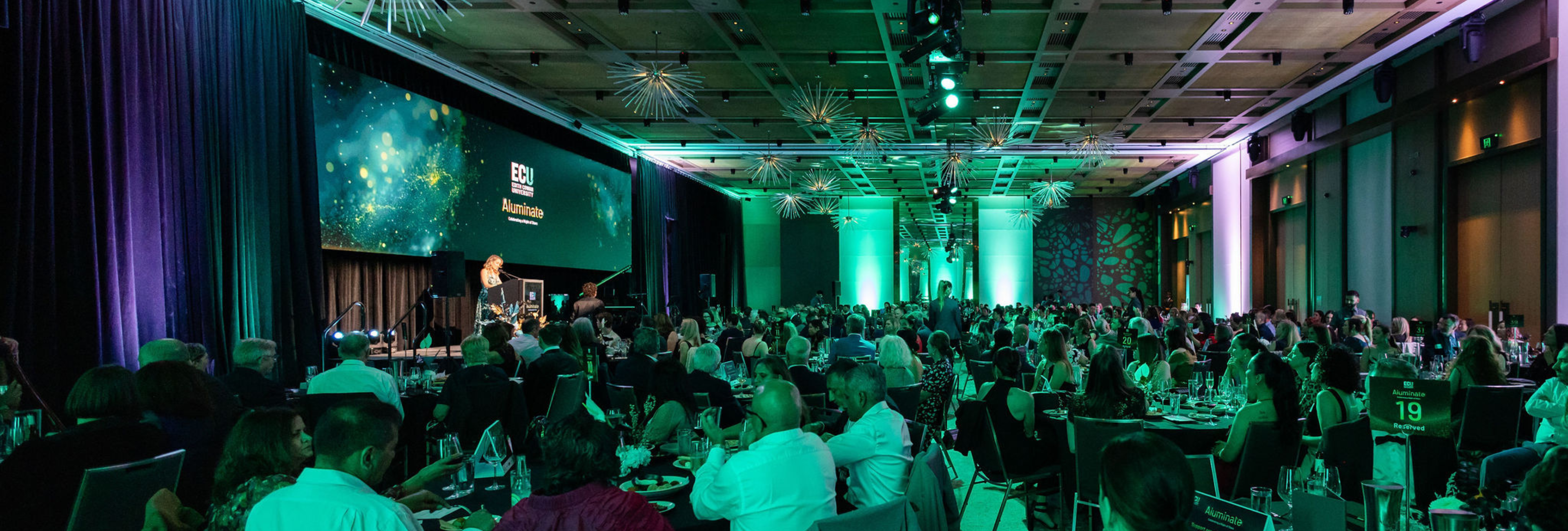 Full room of attendees at Aluminate 2025 with MC Cassie Silver on stage