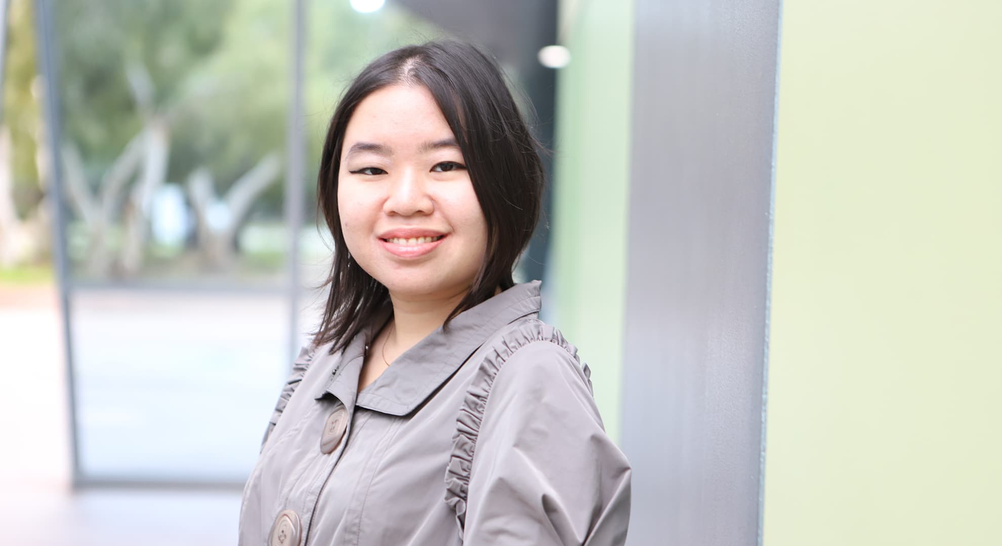 Alberta Natasia Adji (Tasia) has shoulder-length black hair and wears a brown blouse, she grins towards the camera for her headshot.