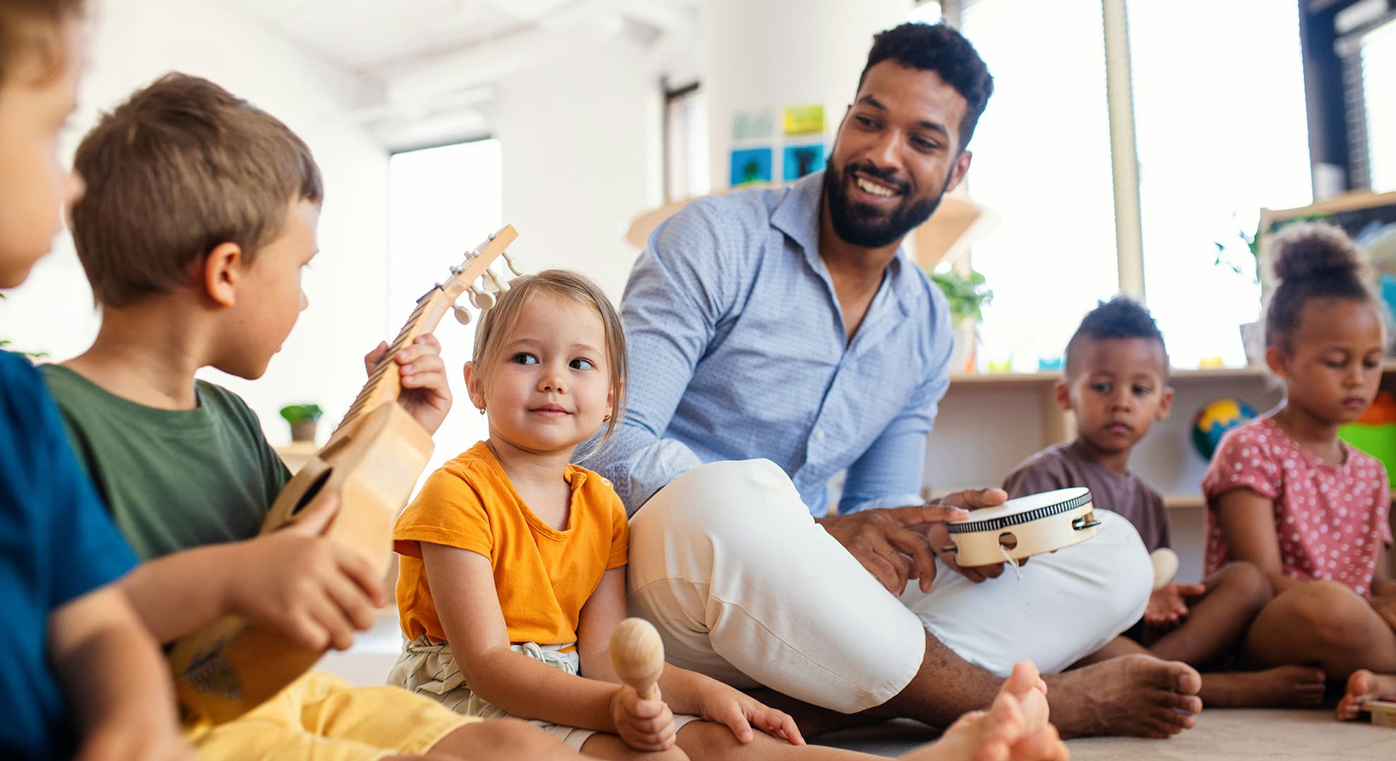 Music teacher sitting on mat playing instruments with young children