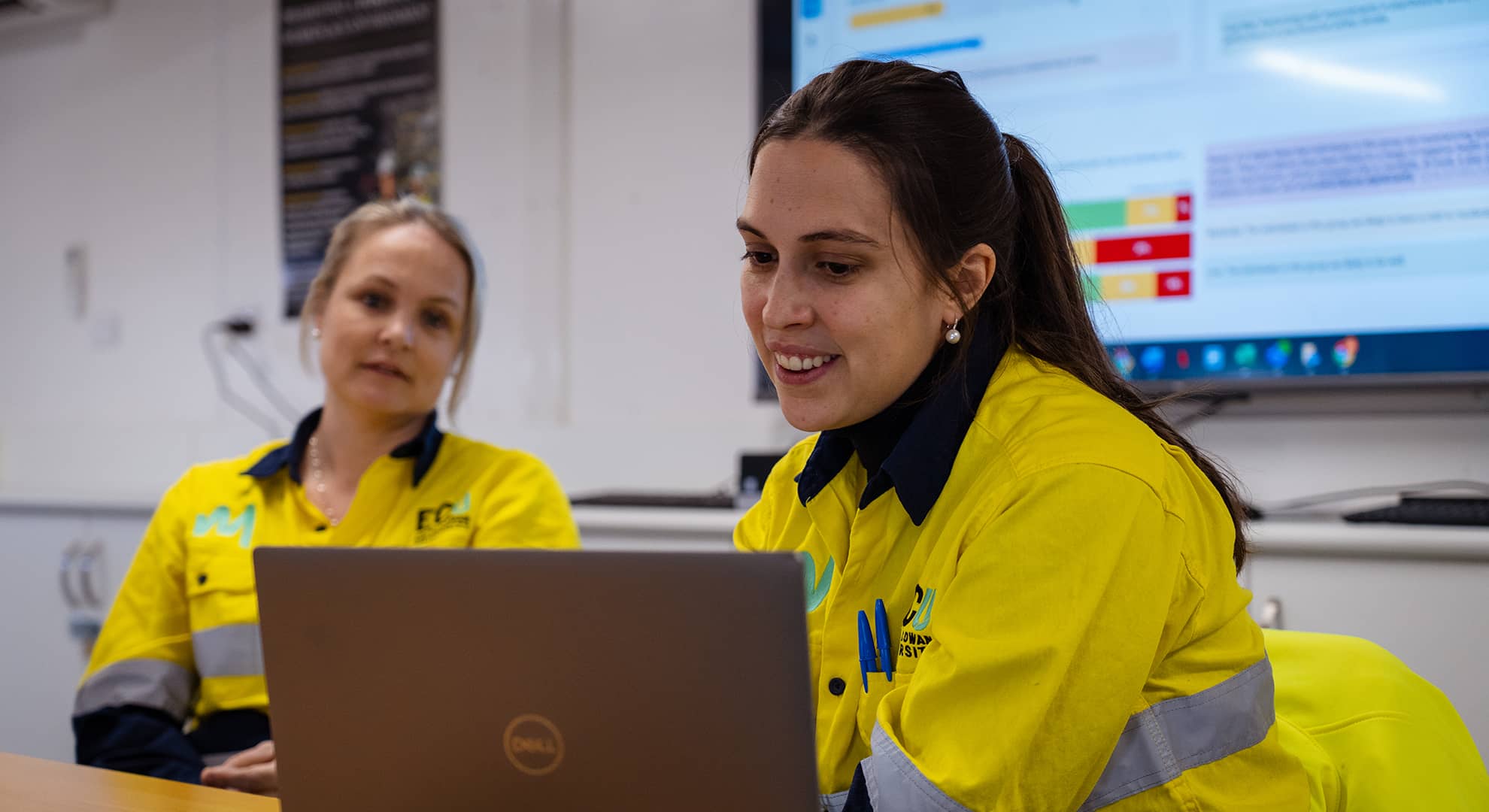 Two women in high-vis gear sitting in front of a laptop.