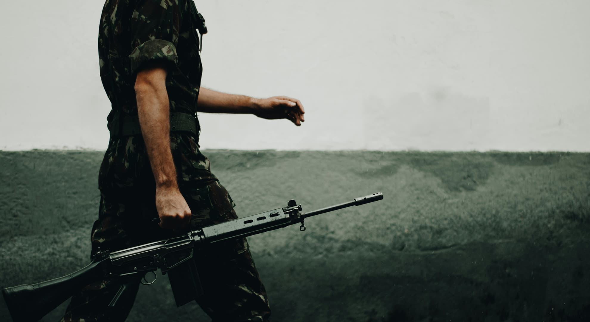 Man in military uniform walking with a gun.