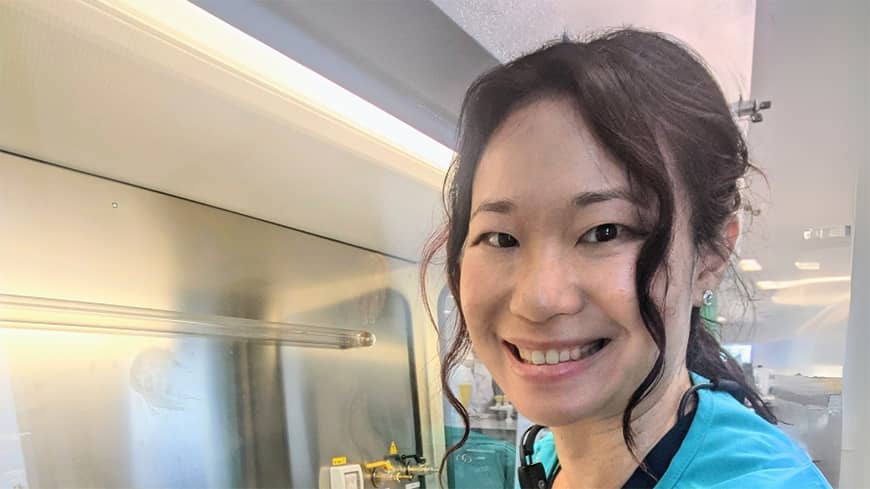 A woman in blue scrubs sitting in front of a medical station.