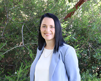 A portrait photo of Mrs Nadia Hunt, smiling and standing in front of trees.