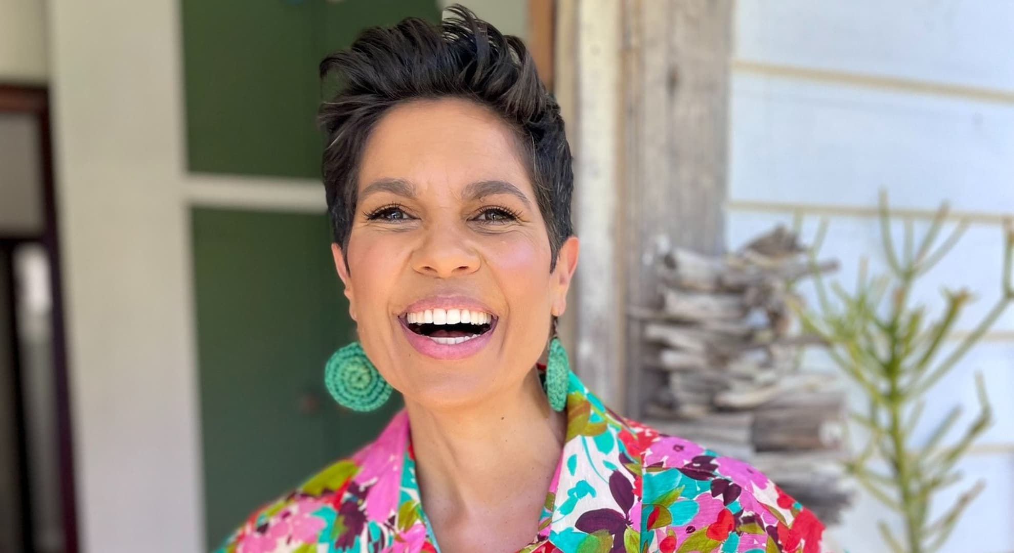 Head and shoulders photo of smiling person with short styled dark brown hair in bright patterned blouse