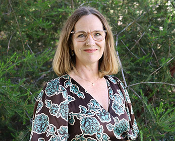 A portrait of Ms Wendy Harmon smiling and standing in from of a tree.