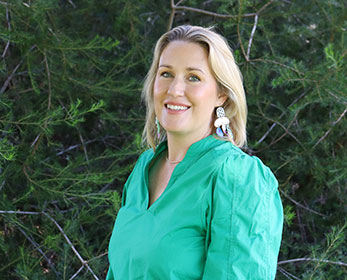 A portrait image of Mrs Susan McMahon smiling at the camera and standing in front of a tree