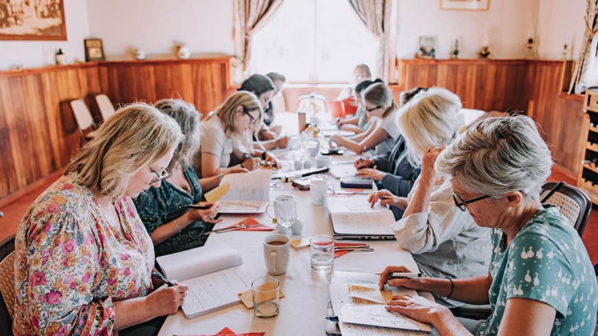 A group of people sitting at a large table writing in notebooks