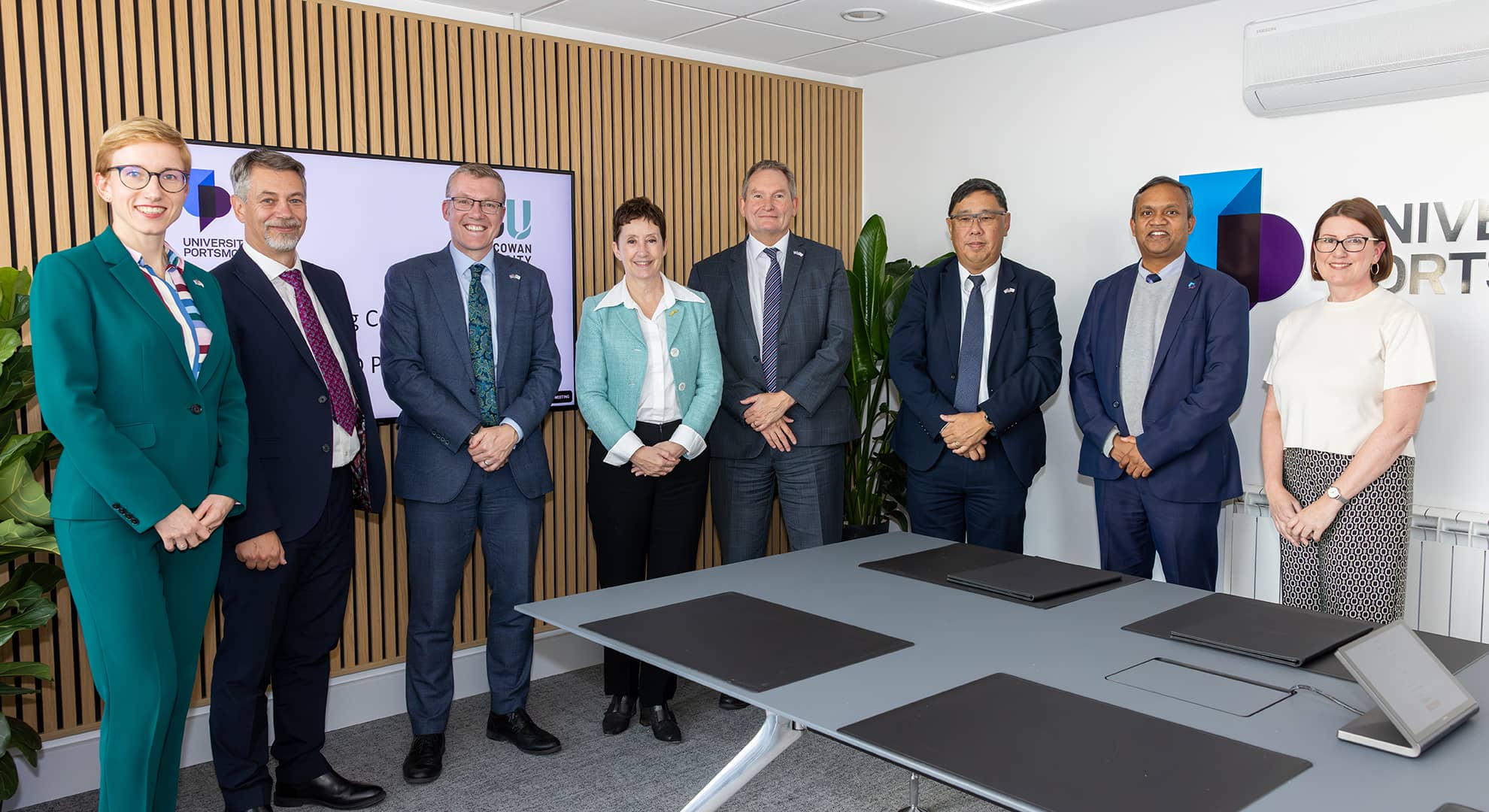 A group of eight people stood in a boardroom facing the camera