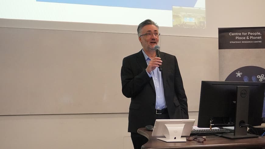 Professor Arshad Omari holds a microphone at the front and welcomes the audience.