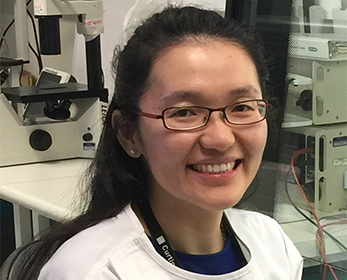 Image of a woman smiling wearing glasses in a white labcoat