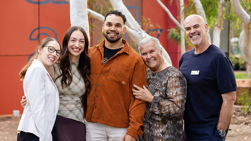 A group shot of five people standing close to each other smiling for the camera 