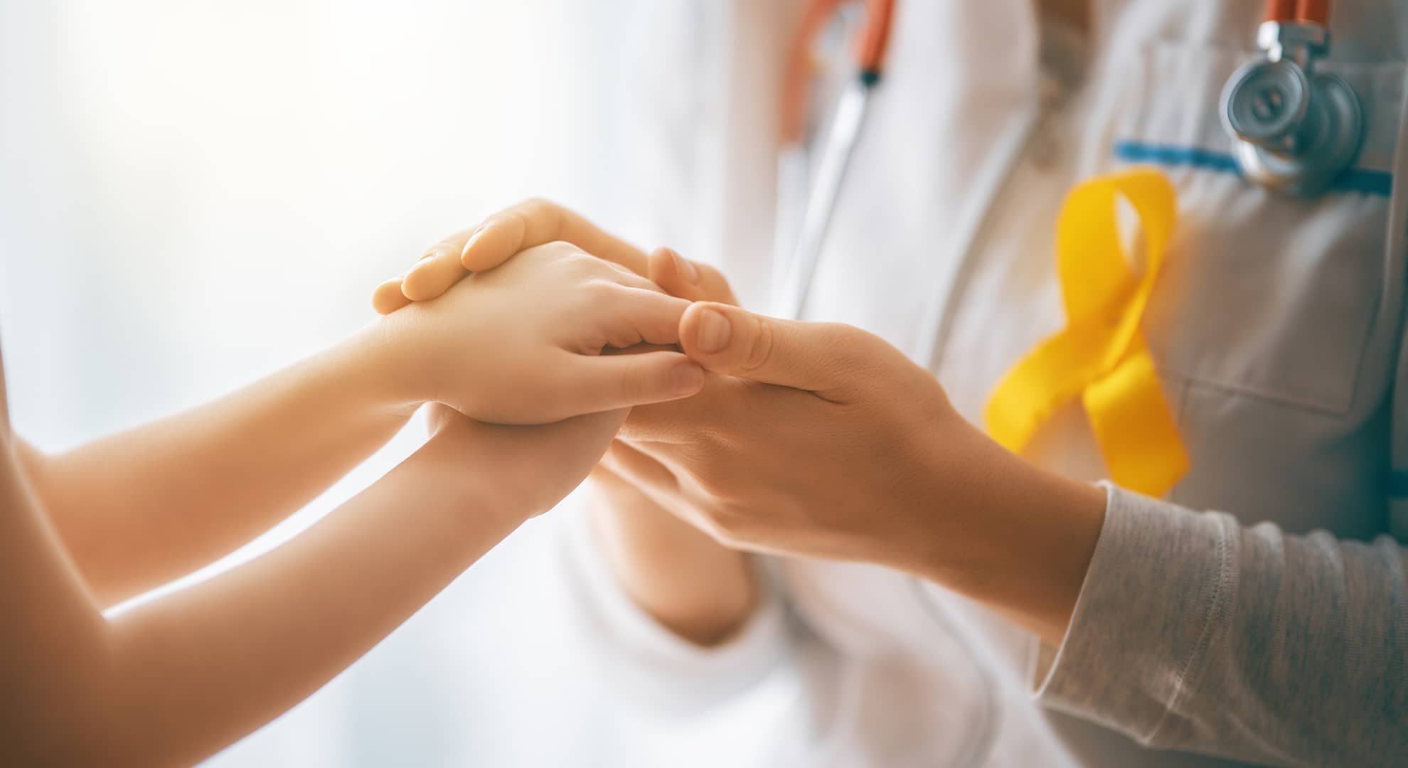 Woman in doctor's coat holding the hands of a child.