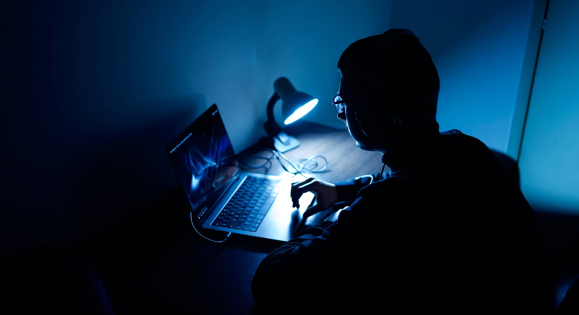 Young person looking at laptop in dark room.
