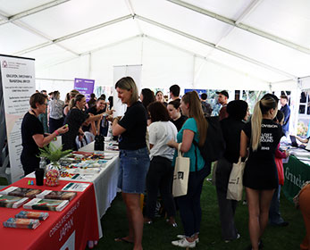 Students interacting with partners at their stalls at the school of education careers fair holding tote bags, smiling and talking.