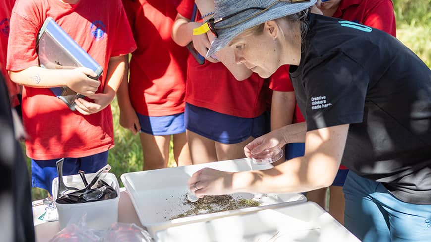 A woman leaning over a table with white containers, surrounded by children.