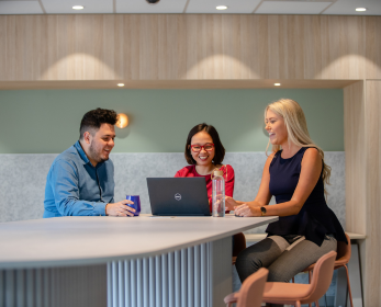 Three ECU researchers sitting together at a table, smiling and working collaboratively on a laptop.