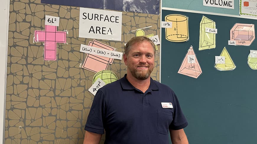Carl Keogh wears a dark blue polo shirt in the classroom.