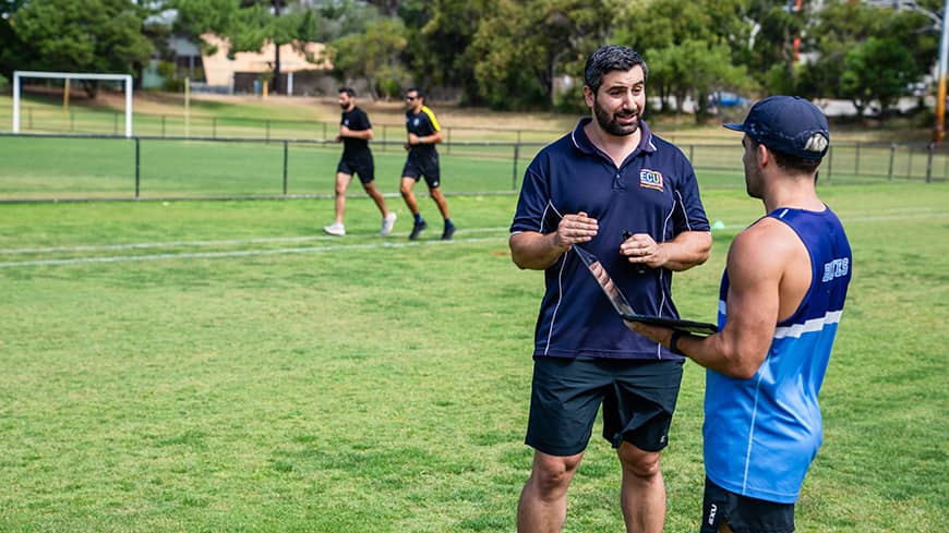 Two men talking with a laptop, while others run.