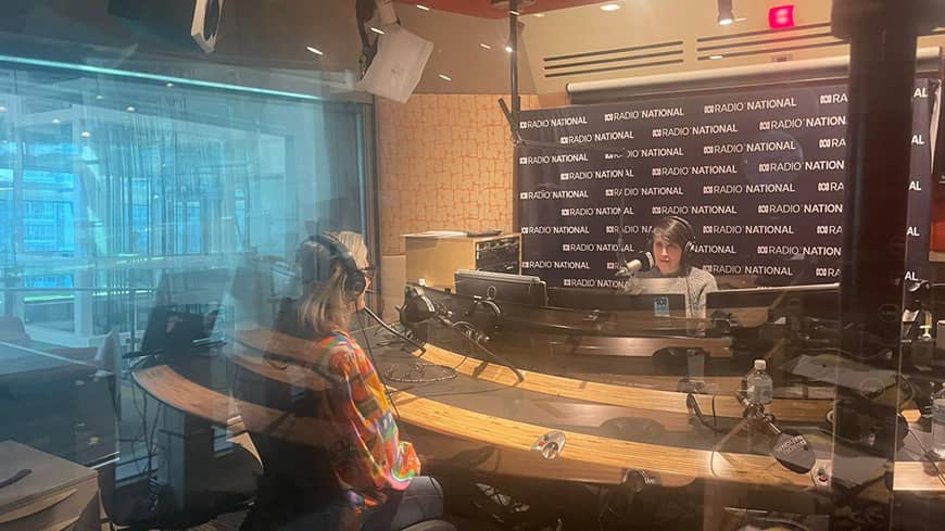 Two people sit opposite each other in a radio studio