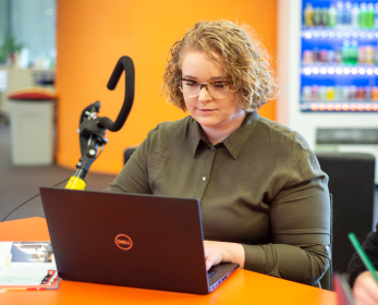 Student using a laptop at ECU Library with a mobility aid nearby and a vending machine in the background.