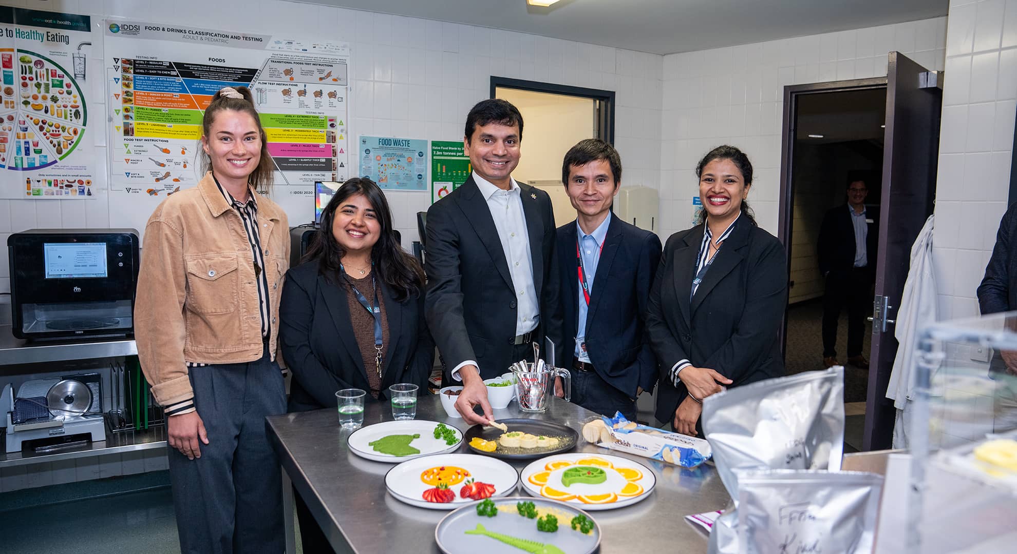 Five people standing behind a table with food.