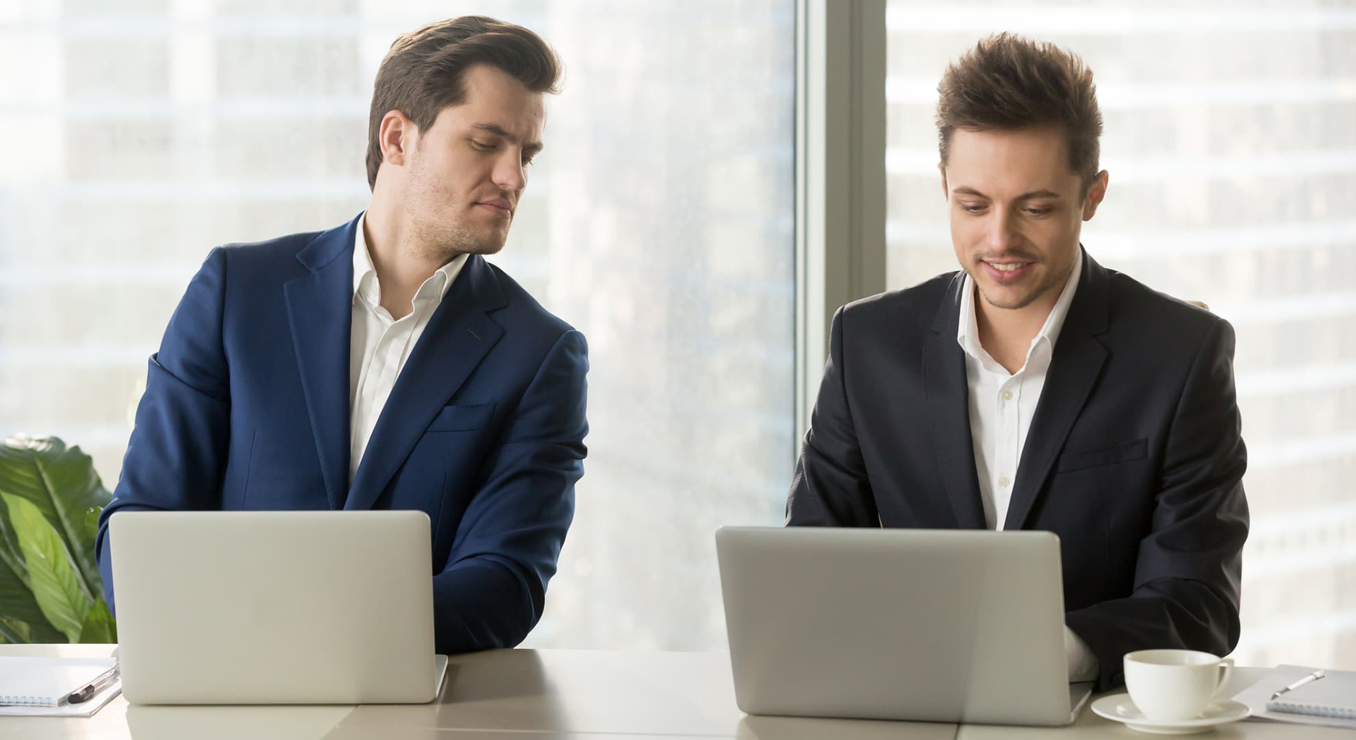 Two men sitting next to each other, with laptops.