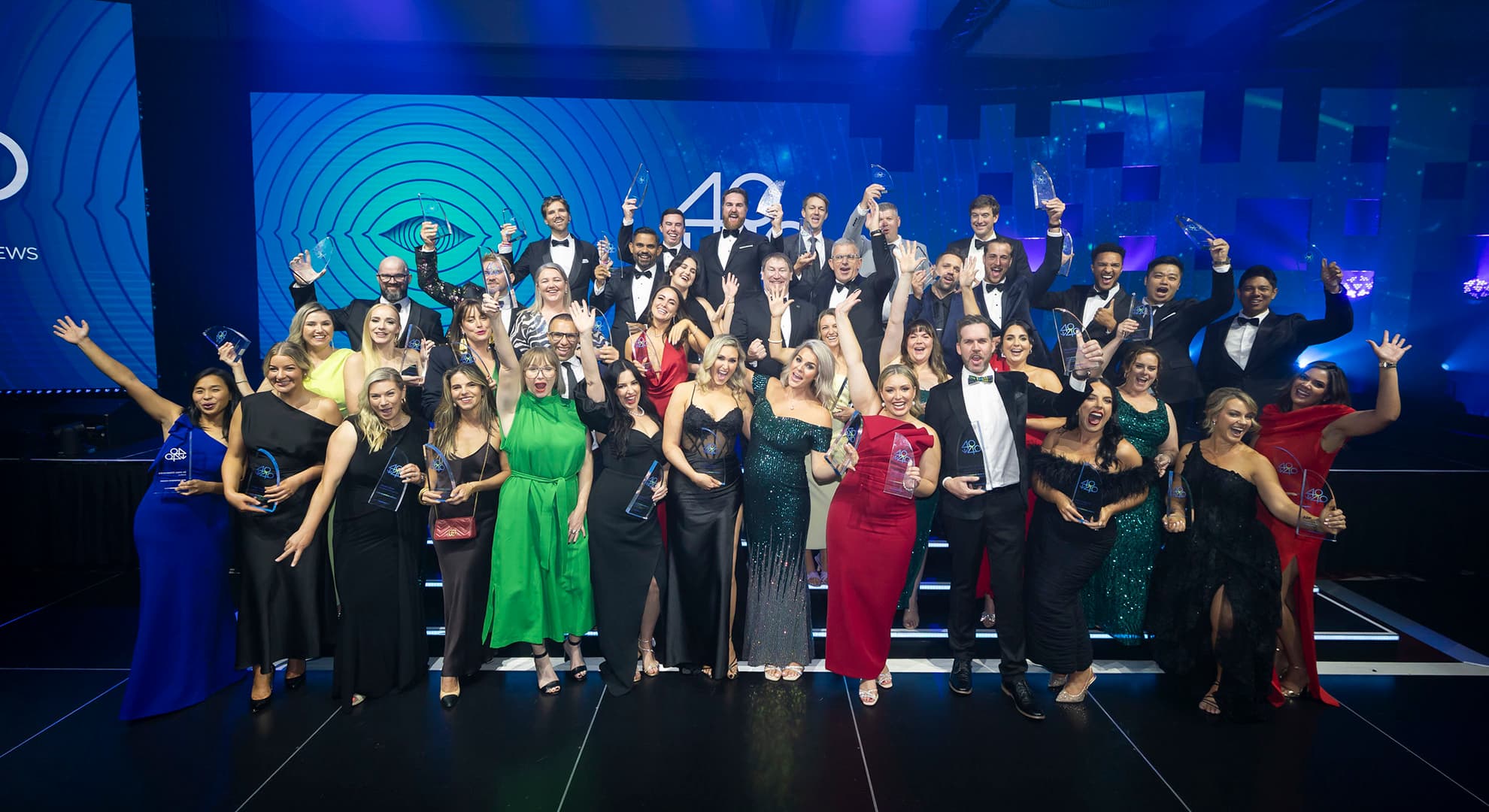 Large group of people in cocktail wear on stage cheering with their awards held up