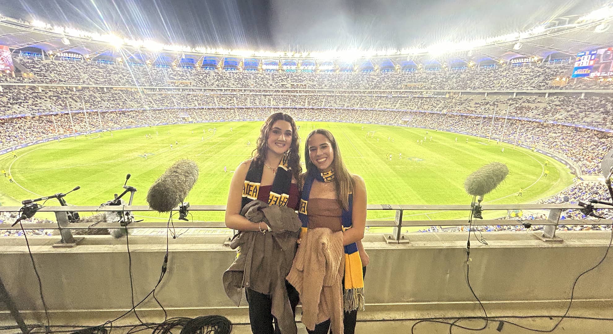 Two people standing on the media deck with a full stadium behind them