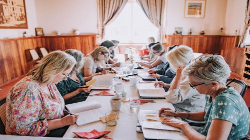 A group of people sitting at a large table writing in notebooks