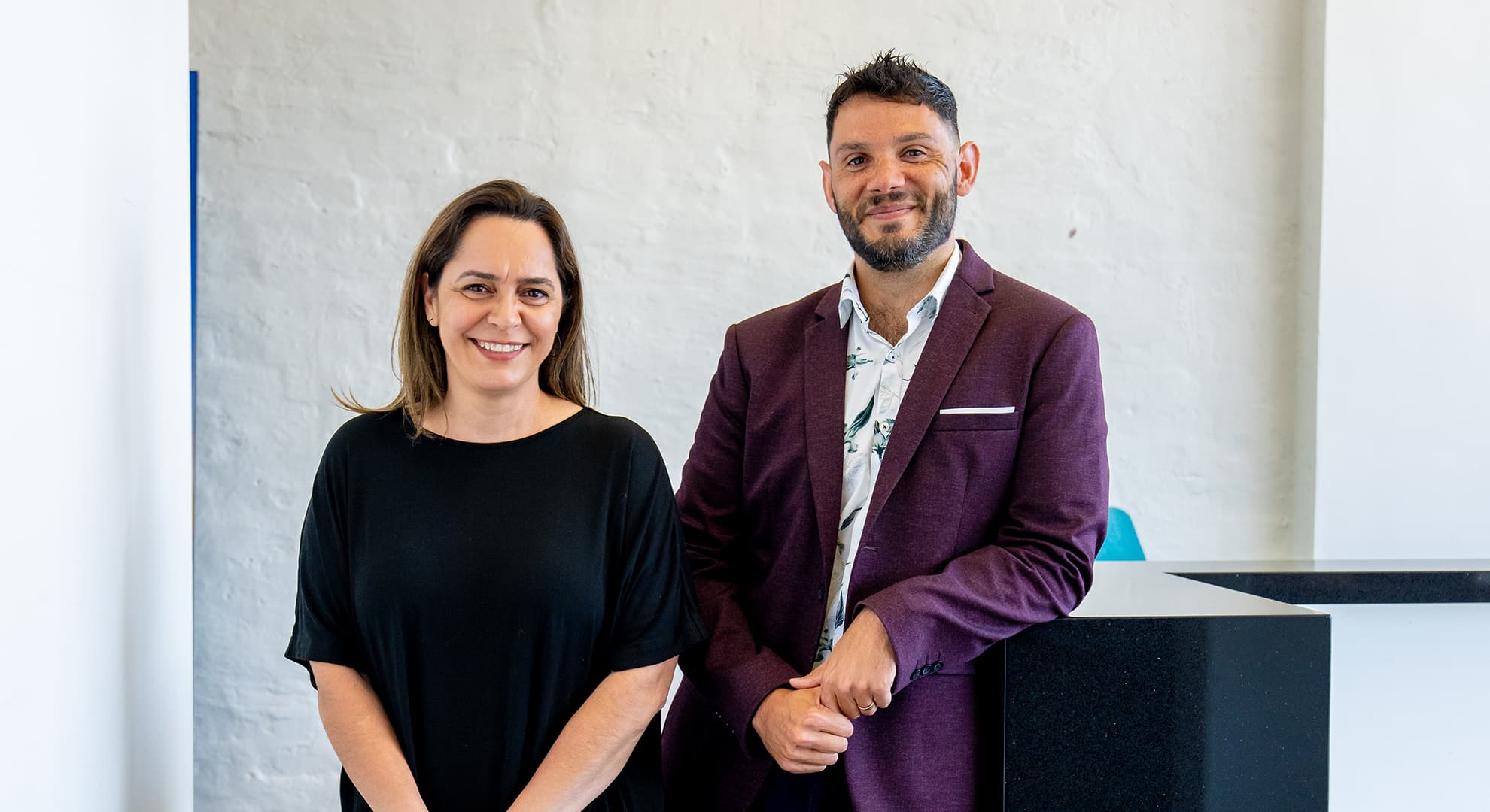 Two people smiling standing in a corridor.