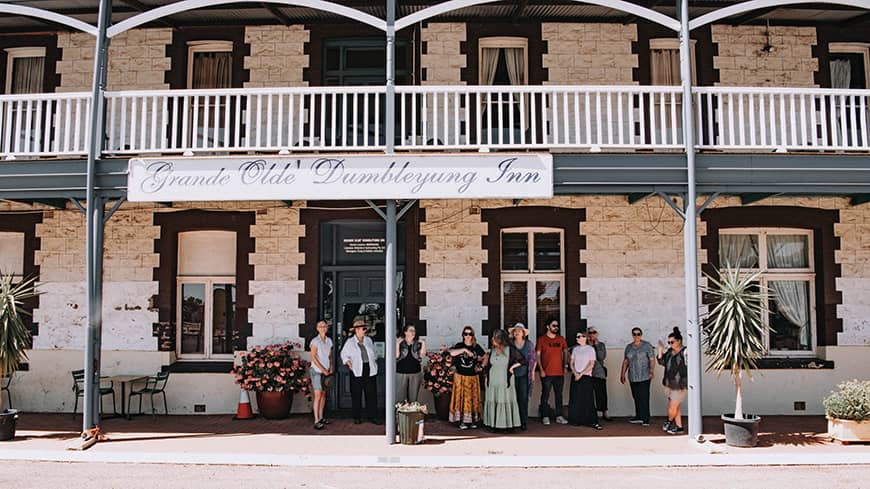 A group of people standing under the wide verandah of a heritage brick building