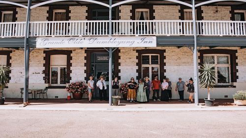 A group of people standing under the wide verandah of a heritage brick building