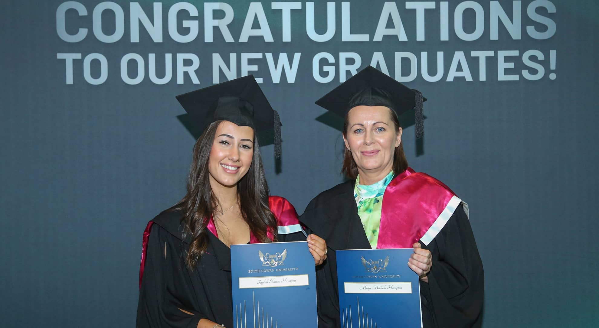 Two woman standing with degrees