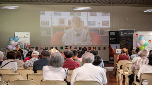A group of people on chairs watch a large screen on a wall