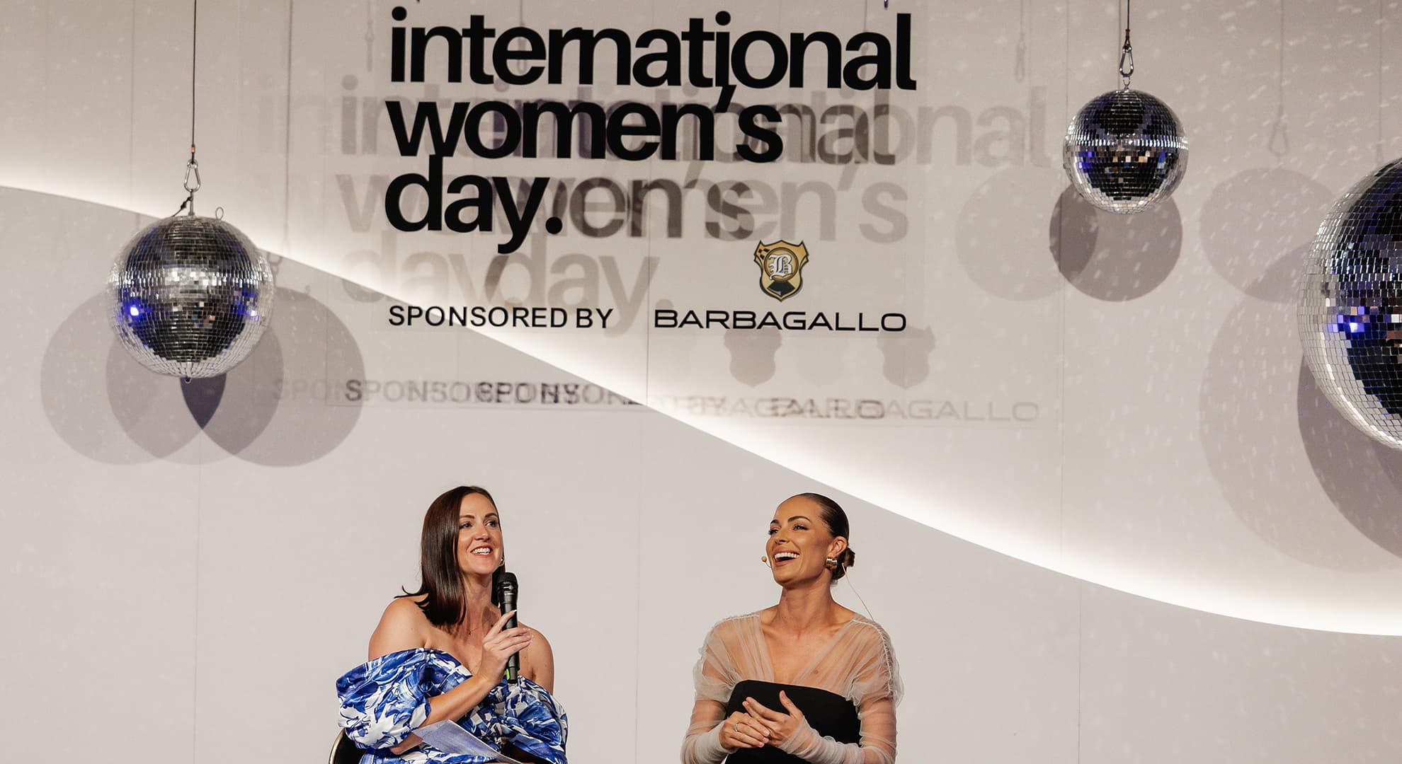 Two people talking on stage with International Women's Day Perth event backdrop.