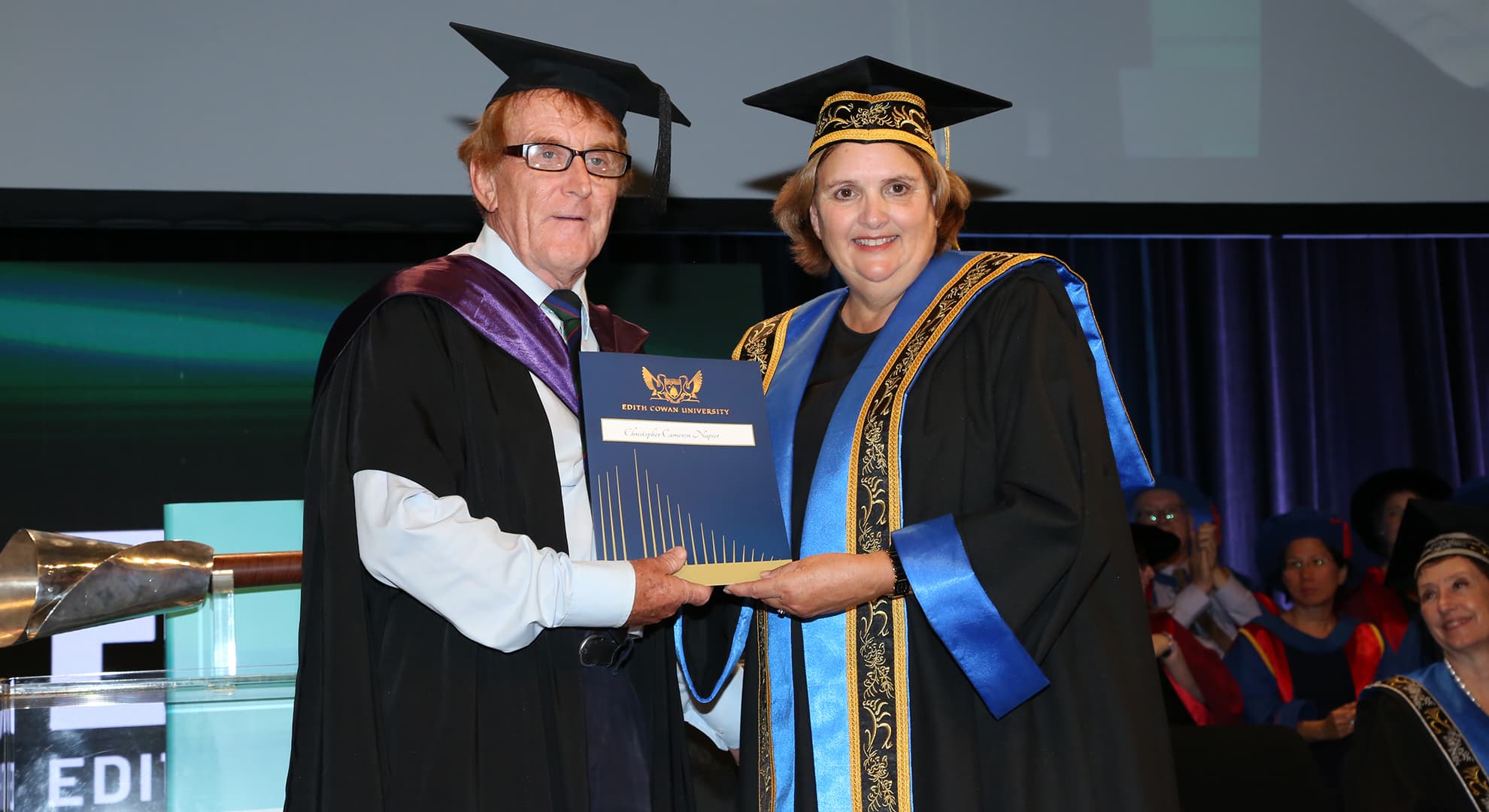A older man receiving a degree from a woman