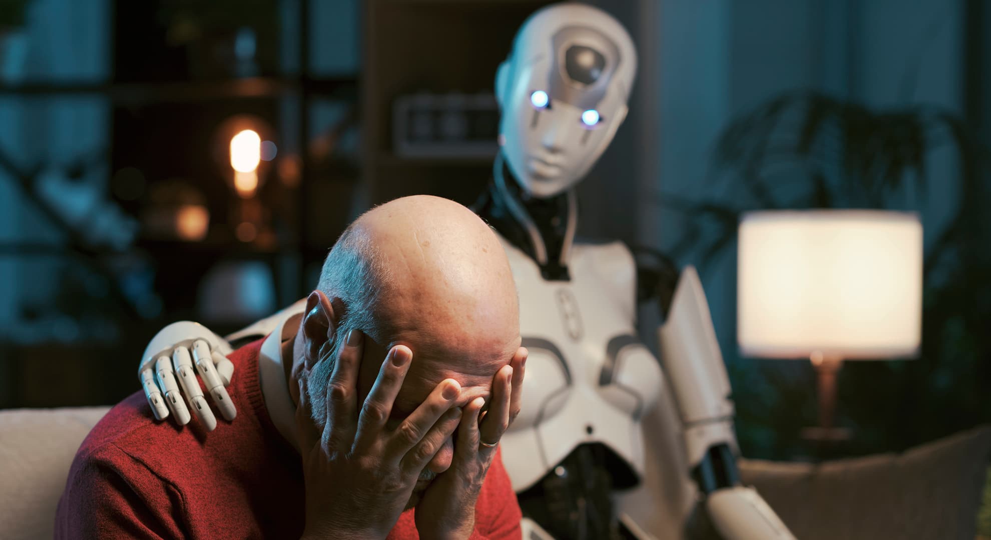 Robot comforting man in red jumper.