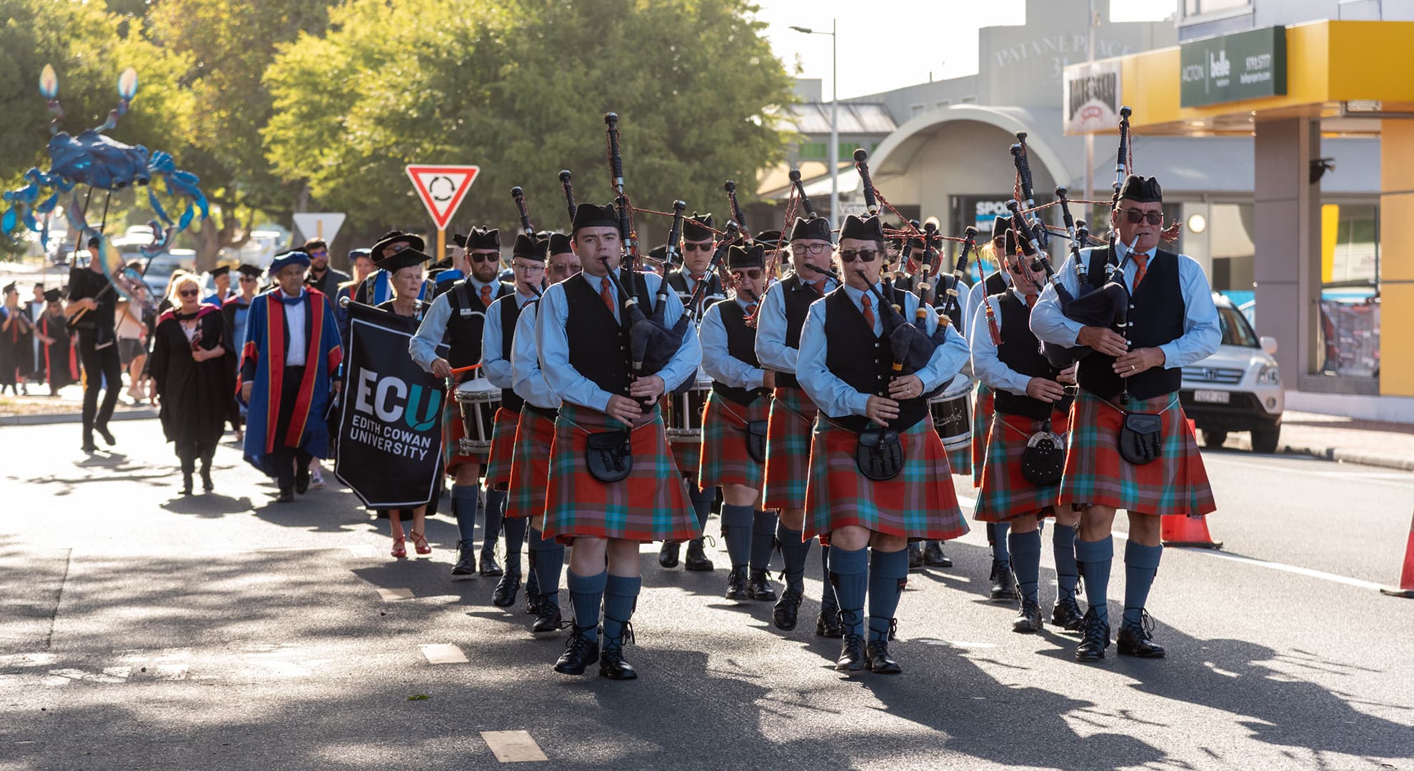 Men in kilts playing instruments followed by a procession of students, academics and children